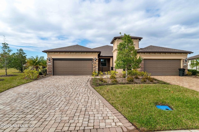 prairie-style home featuring a garage, stone siding, decorative driveway, a front yard, and stucco siding