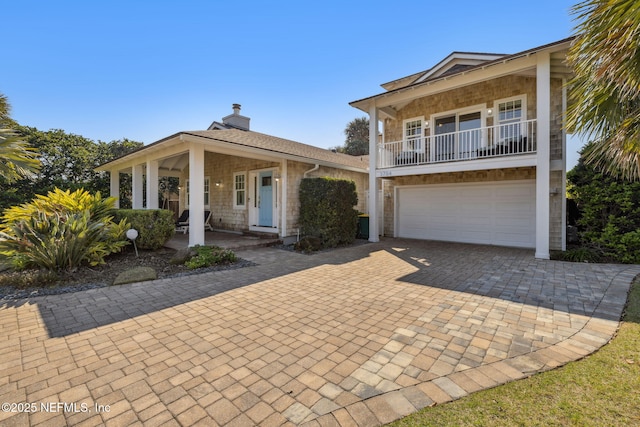 view of front of property featuring a porch, an attached garage, a balcony, decorative driveway, and a chimney