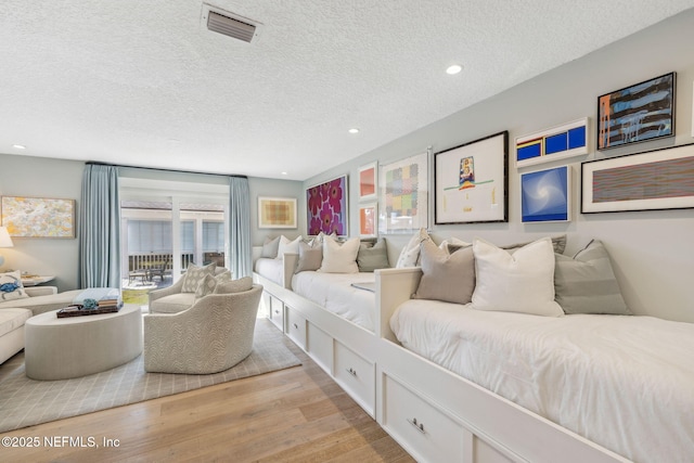 bedroom featuring light wood finished floors, visible vents, a textured ceiling, and recessed lighting