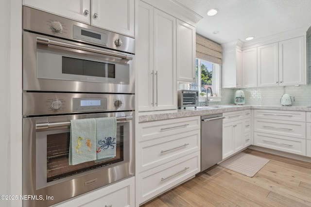 kitchen featuring stainless steel appliances, light wood finished floors, backsplash, and white cabinetry