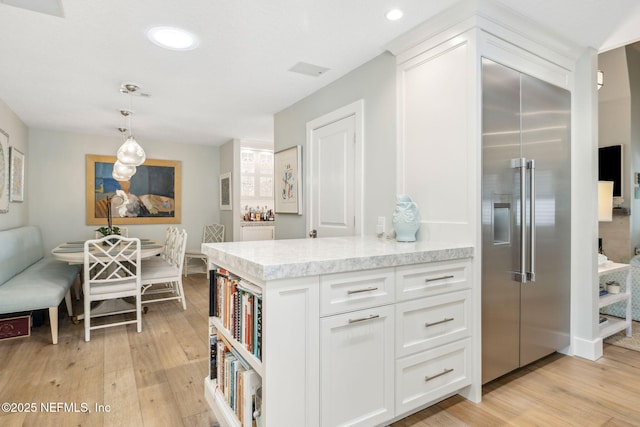 kitchen with light stone countertops, stainless steel built in fridge, light wood finished floors, and white cabinetry