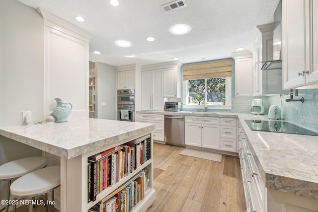 kitchen with light wood finished floors, visible vents, appliances with stainless steel finishes, wall chimney range hood, and a kitchen bar