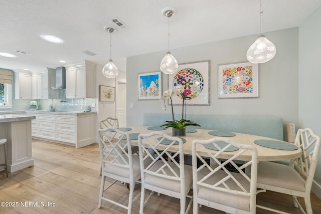 dining space featuring a textured ceiling, light wood-type flooring, and visible vents