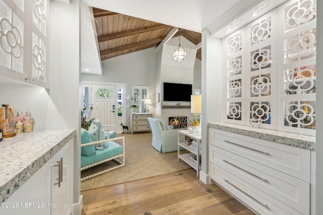 interior space with a warm lit fireplace, high vaulted ceiling, wood ceiling, beam ceiling, and light wood finished floors