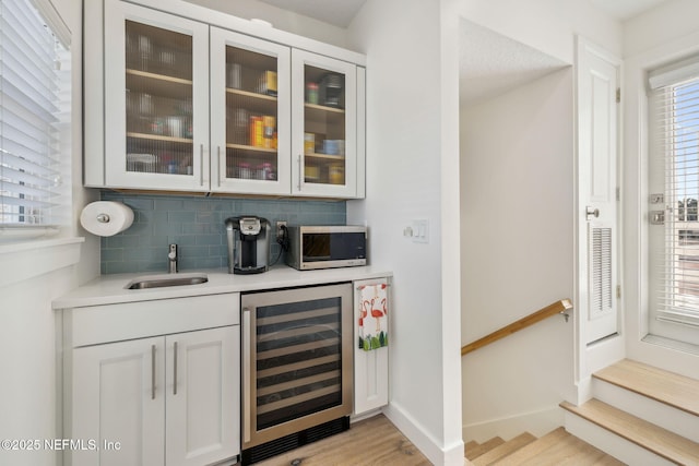 bar with beverage cooler, baseboards, stainless steel microwave, a sink, and backsplash