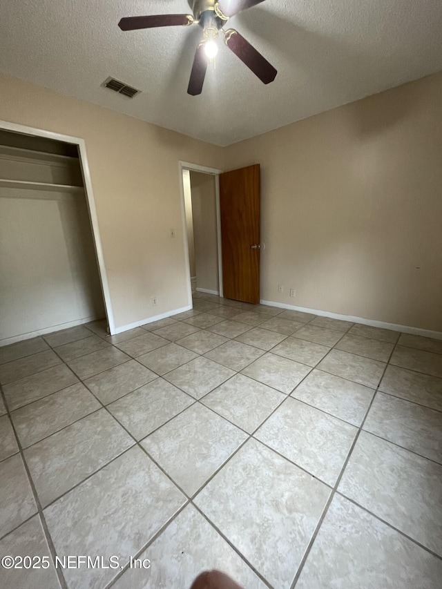 unfurnished bedroom featuring a textured ceiling, light tile patterned floors, visible vents, baseboards, and a closet