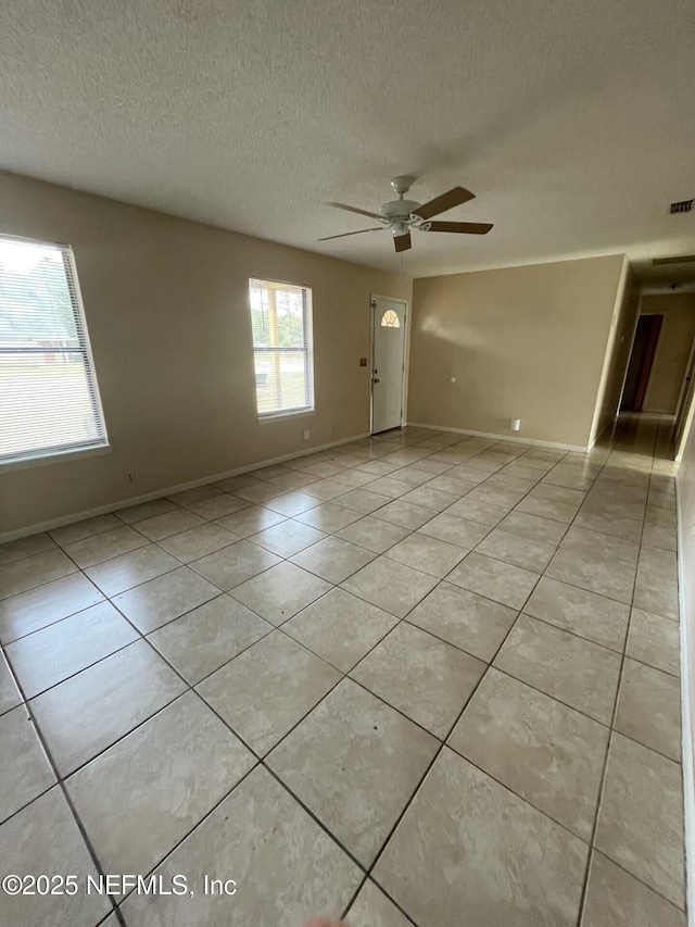 spare room with a textured ceiling, light tile patterned flooring, a ceiling fan, and baseboards