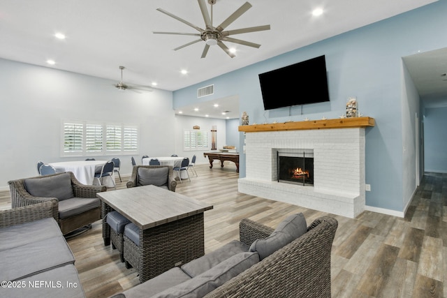 living room featuring a brick fireplace, visible vents, a ceiling fan, and wood finished floors