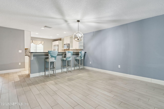 kitchen with decorative light fixtures, stainless steel microwave, white cabinetry, a peninsula, and a kitchen bar