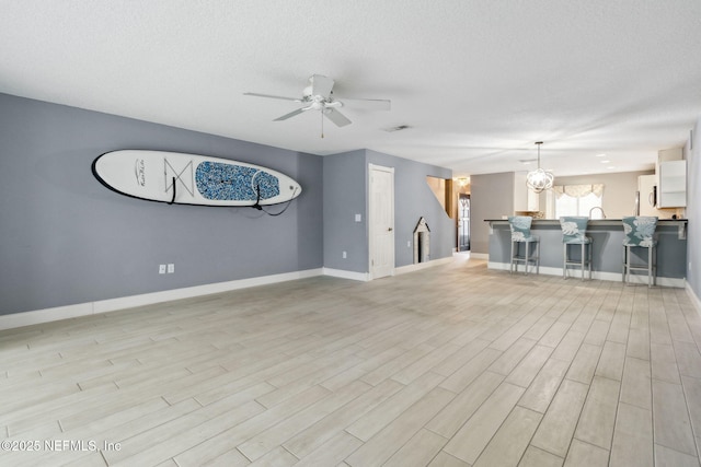 unfurnished living room with baseboards, a textured ceiling, light wood-style flooring, and a ceiling fan