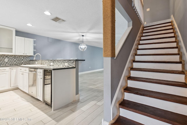 kitchen with visible vents, hanging light fixtures, stainless steel dishwasher, white cabinetry, and a sink