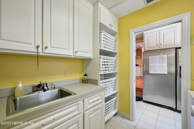 kitchen featuring light tile patterned floors, white cabinets, freestanding refrigerator, light countertops, and a sink