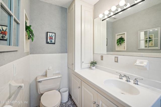 bathroom with wainscoting, toilet, a textured ceiling, vanity, and tile walls