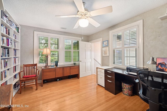 office with light wood-style floors, a textured ceiling, visible vents, and a ceiling fan