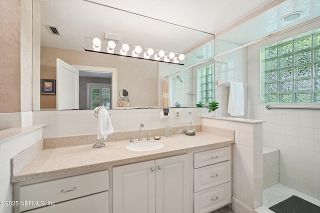 bathroom with plenty of natural light, visible vents, a walk in shower, and vanity