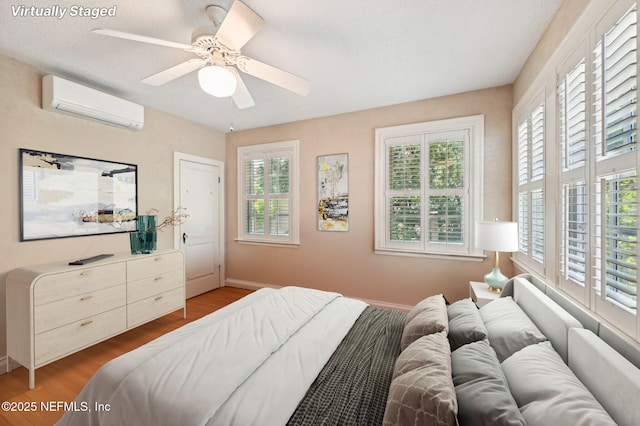 bedroom with a ceiling fan, a wall unit AC, baseboards, and wood finished floors