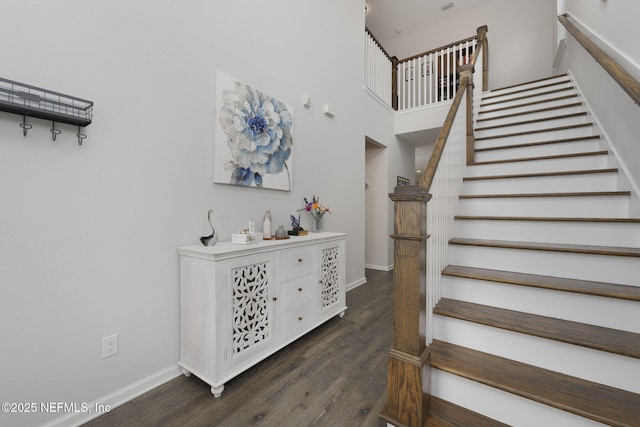 stairway with a high ceiling, baseboards, and wood finished floors