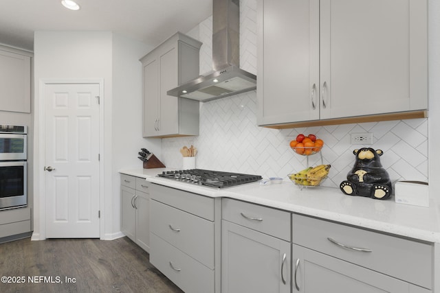 kitchen featuring wall chimney exhaust hood, appliances with stainless steel finishes, light stone counters, and gray cabinetry