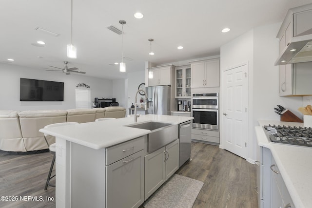 kitchen with an island with sink, appliances with stainless steel finishes, light countertops, and decorative light fixtures