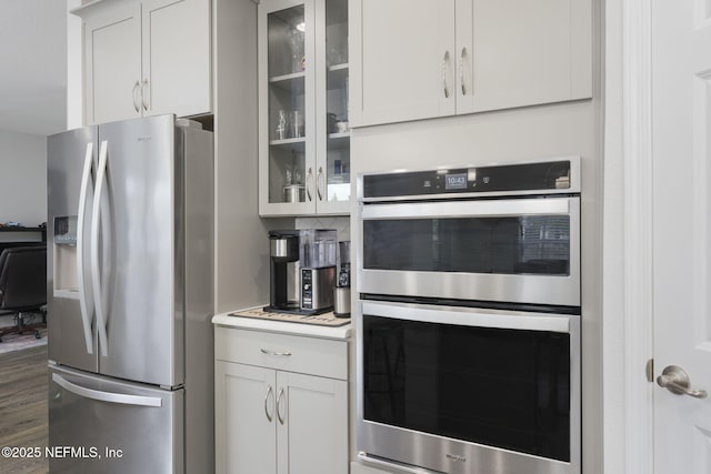 kitchen with white cabinets, light countertops, appliances with stainless steel finishes, dark wood-style floors, and glass insert cabinets