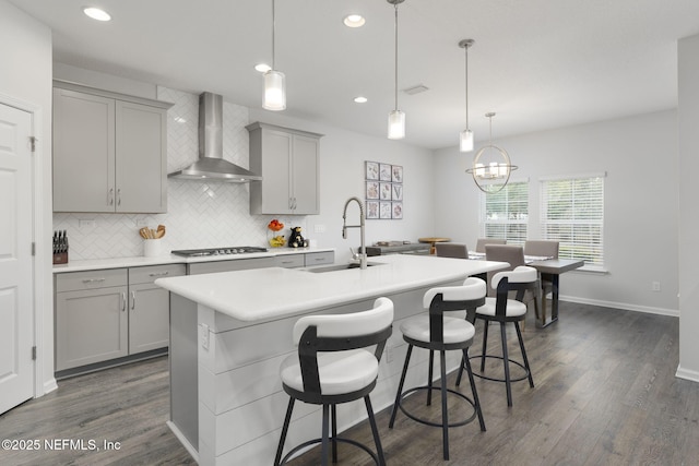 kitchen featuring decorative light fixtures, light countertops, a sink, an island with sink, and wall chimney exhaust hood