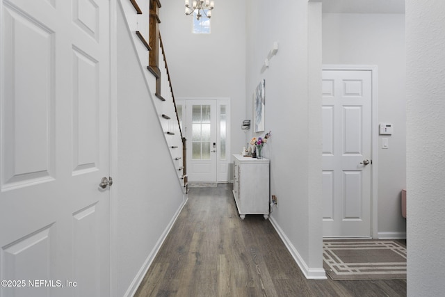 corridor with dark wood-style floors, a chandelier, a high ceiling, and baseboards