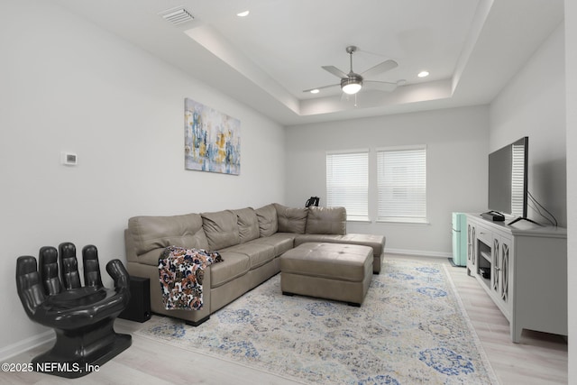 living room featuring light wood-style flooring, recessed lighting, visible vents, baseboards, and a tray ceiling