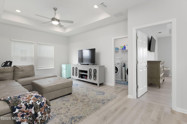 living area featuring baseboards, visible vents, light wood-style flooring, ceiling fan, and a tray ceiling