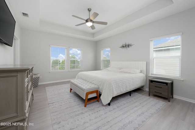 bedroom featuring light wood-style floors, a raised ceiling, visible vents, and baseboards