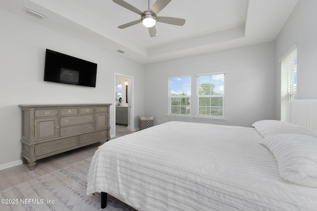 bedroom with light wood-style flooring, multiple windows, visible vents, and a raised ceiling