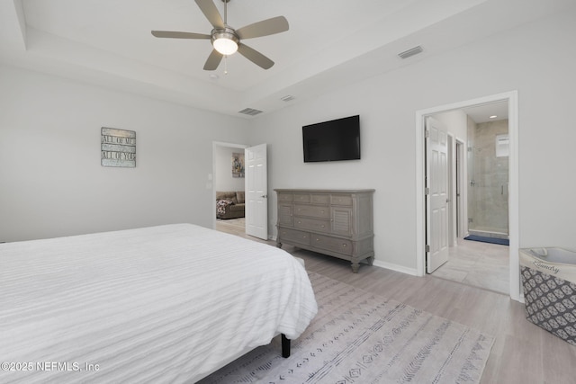 bedroom with connected bathroom, visible vents, baseboards, light wood-type flooring, and a raised ceiling