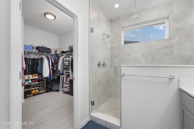 bathroom with a stall shower, a walk in closet, vanity, and wood finished floors