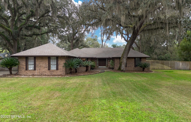 single story home with brick siding, a shingled roof, a front yard, and fence