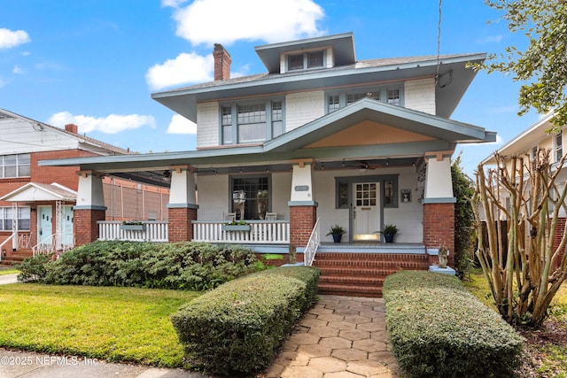 american foursquare style home with covered porch, brick siding, and a front lawn