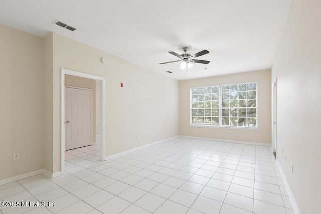 empty room with ceiling fan, light tile patterned flooring, visible vents, and baseboards