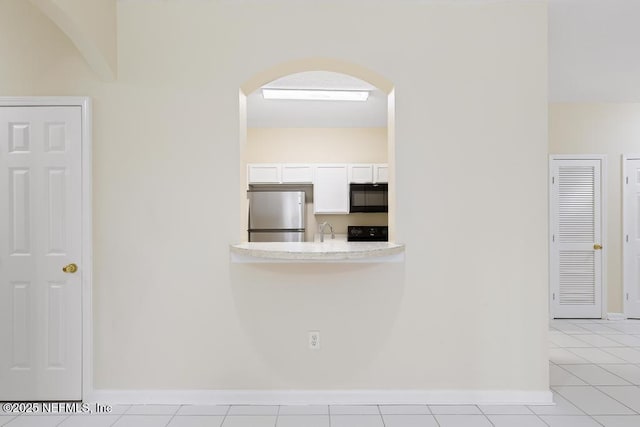 kitchen featuring black microwave, range with electric cooktop, stainless steel refrigerator, light countertops, and white cabinetry