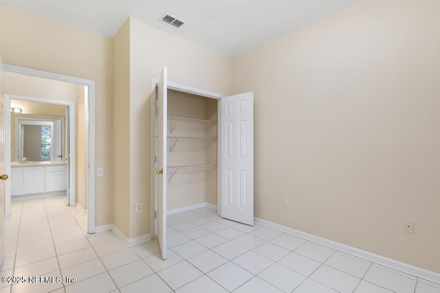 unfurnished bedroom featuring a closet, light tile patterned flooring, visible vents, and baseboards