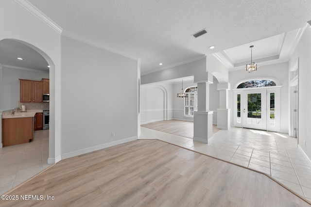 entryway with decorative columns, visible vents, a textured ceiling, light wood-style floors, and a chandelier