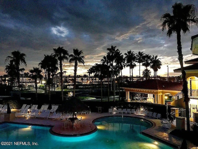 pool at dusk featuring a patio area and a community pool