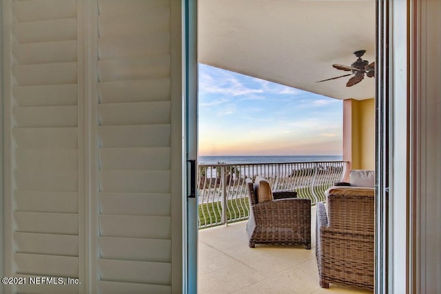 balcony at dusk with a water view and ceiling fan