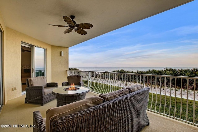 balcony with a fire pit, ceiling fan, a water view, and a view of the beach