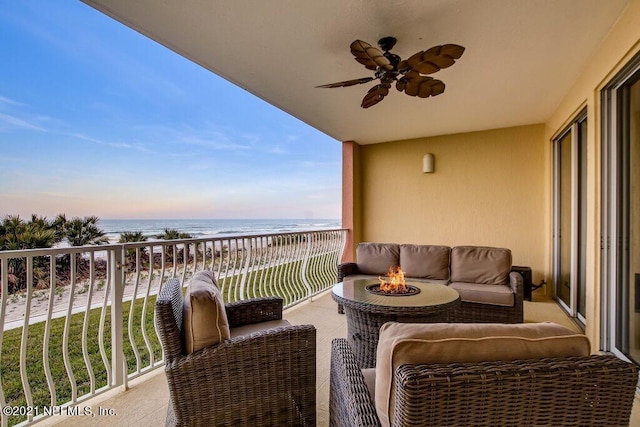 balcony featuring a view of the beach, an outdoor living space with a fire pit, a water view, and ceiling fan