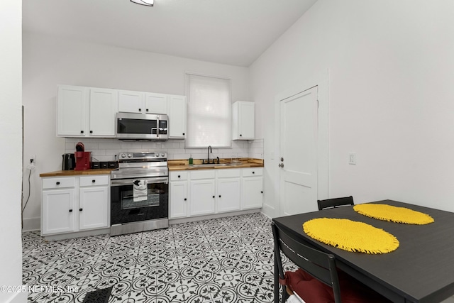 kitchen with wooden counters, appliances with stainless steel finishes, a sink, and white cabinetry