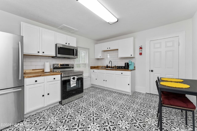 kitchen featuring decorative backsplash, wood counters, appliances with stainless steel finishes, white cabinetry, and a sink