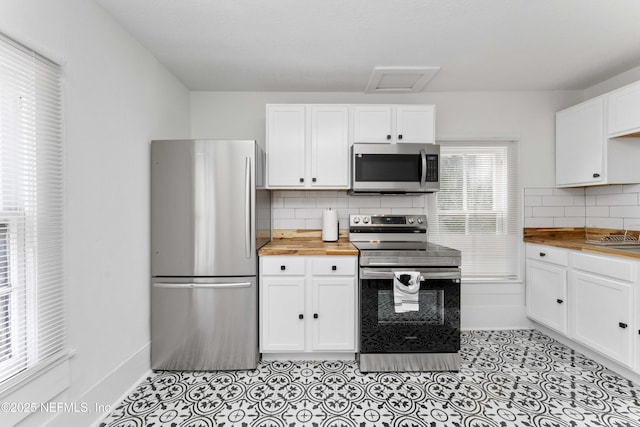 kitchen with white cabinets, butcher block countertops, appliances with stainless steel finishes, backsplash, and light tile patterned flooring