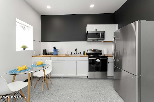 kitchen with decorative backsplash, appliances with stainless steel finishes, white cabinetry, a sink, and wood counters