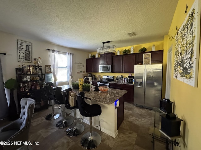 kitchen featuring stainless steel appliances, a kitchen island with sink, dark brown cabinetry, and a kitchen breakfast bar