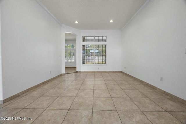 empty room featuring ornamental molding, arched walkways, baseboards, and light tile patterned floors