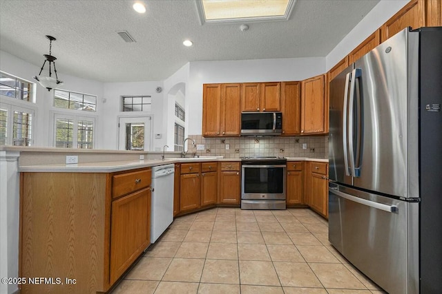 kitchen with stainless steel appliances, brown cabinets, a sink, and backsplash