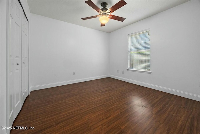 unfurnished bedroom featuring a closet, dark wood finished floors, baseboards, and ceiling fan